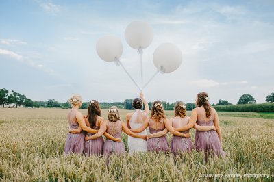 The bridesmaids wear pretty pale purple dresses and pose with bride for a photo in the barley fields at this barn wedding in Cheshire