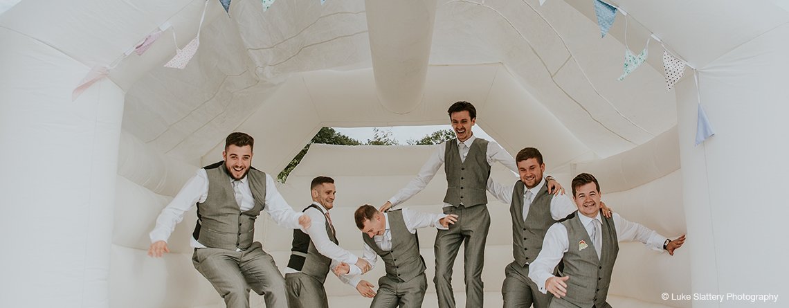 The groomsmen have fun on the bouncy castle at this exclusive use wedding venue