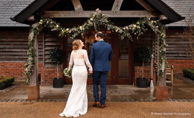 A bride and groom hold hands as they enter the stunning Cheshire wedding barn