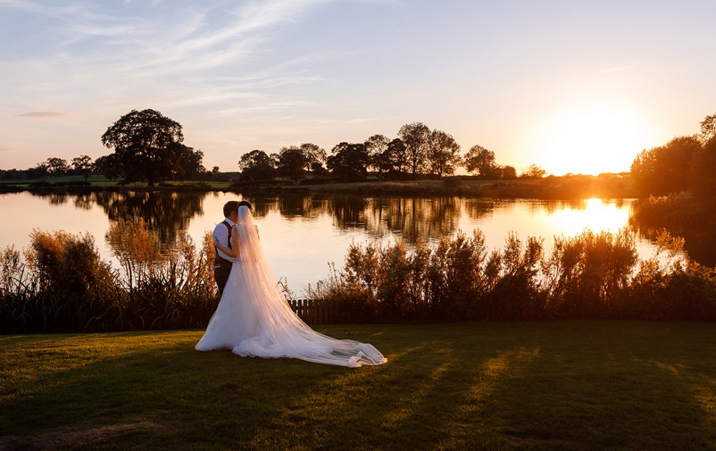 The bride and groom pose for a wedding photo in front of the lake at Sandhole Oak Barn