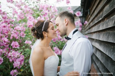 The bride and groom have wedding pictures taken outside the barn with vibrant pink flowers as a backdrop at Sandhole Oak Barn