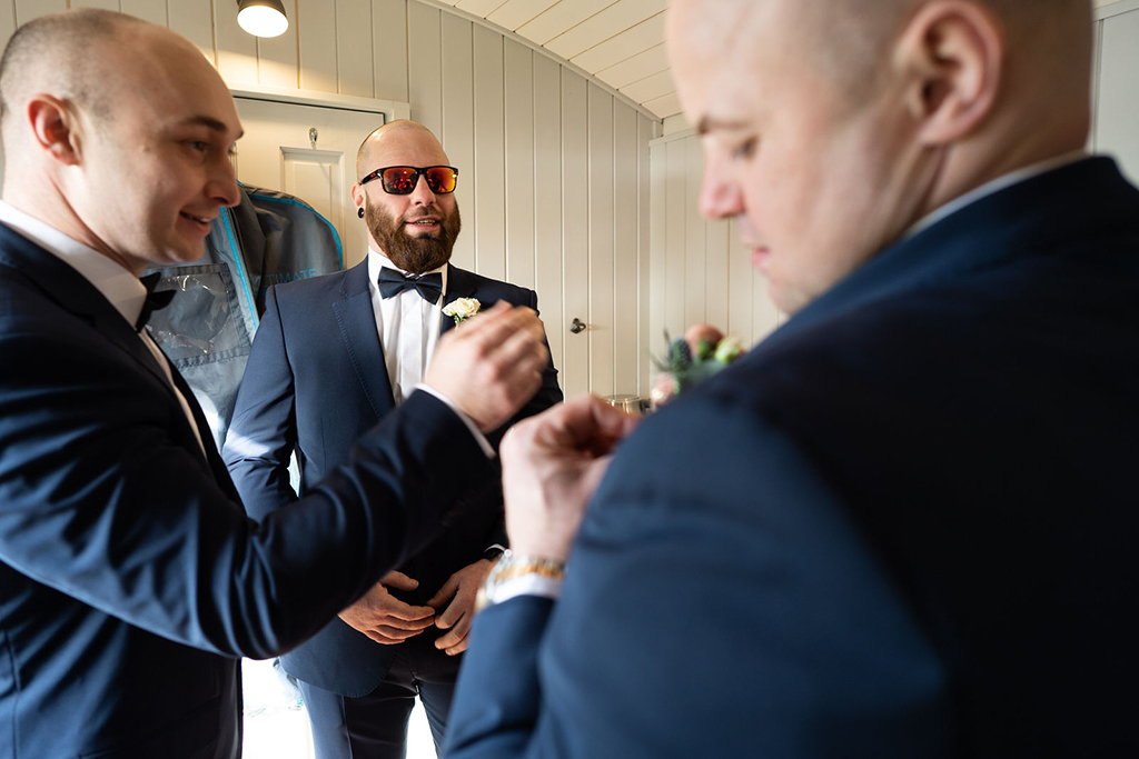 The cool groomsmen apply the finishing touches to their look in the Shepherds Hut preparation room at Sandhole Oak Barn