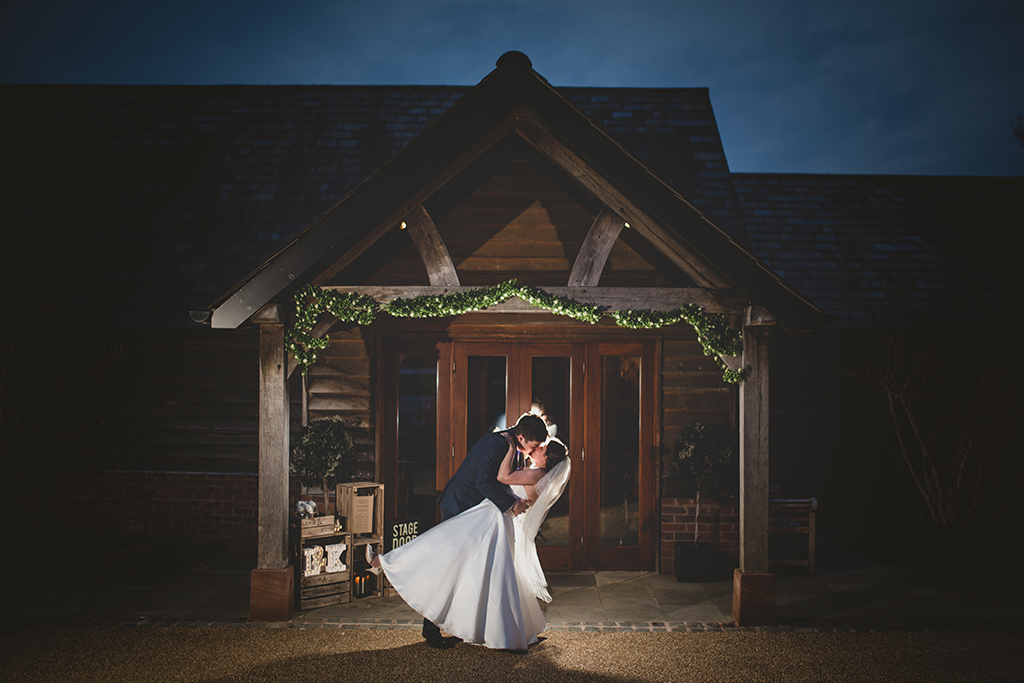 The bride and groom pose for a wedding photo by the entrance to the wedding barn at Sandhole Oak Barn in Cheshire
